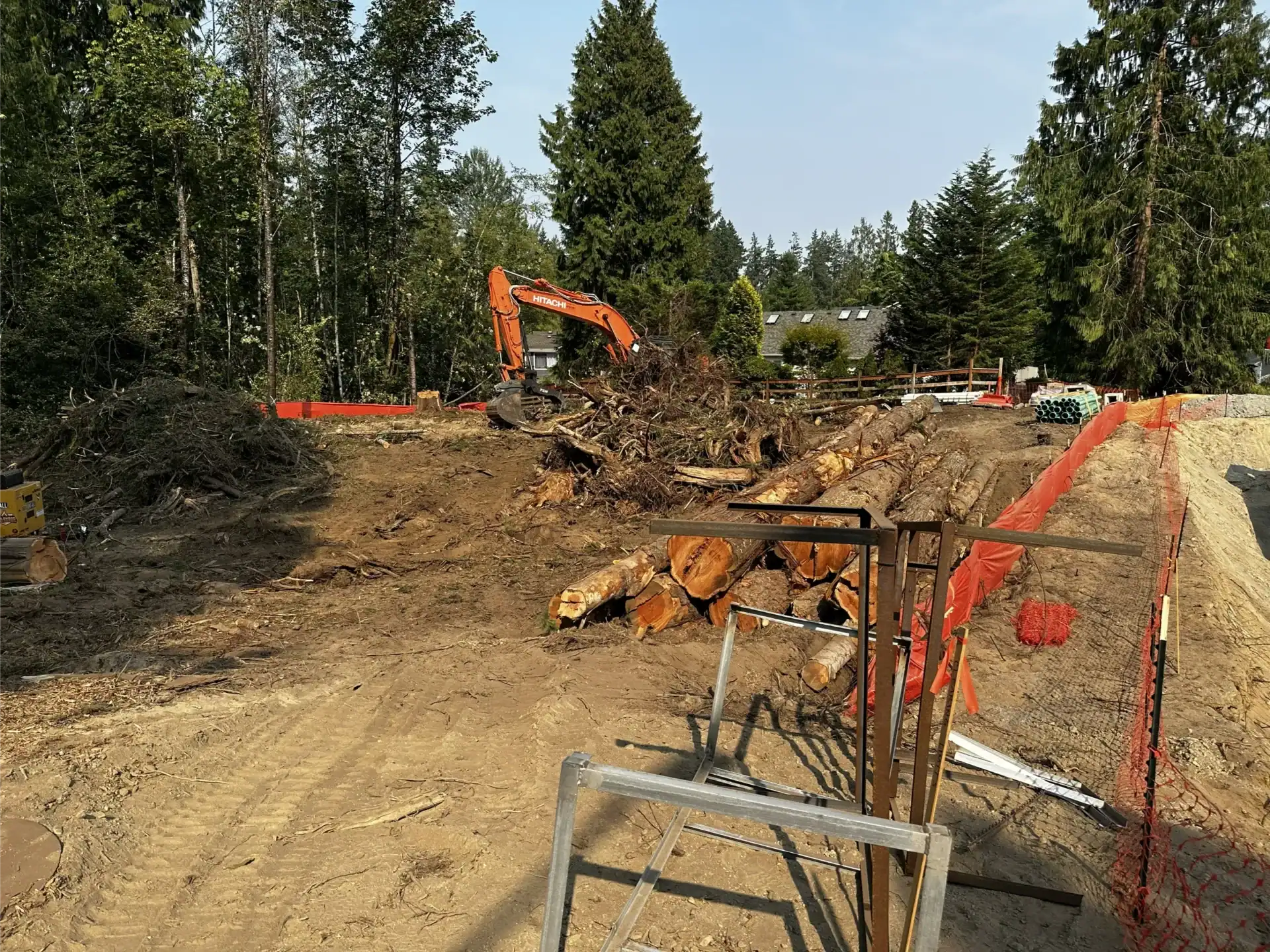 Construction site with an excavator moving debris, cut tree logs on the ground from recent land clearing